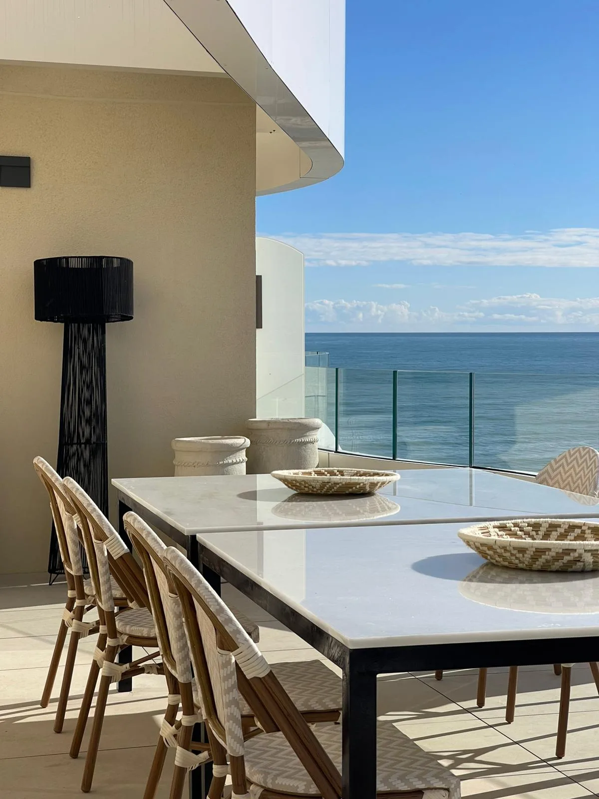 Terraza con mesa de mármol blanco y sillas de fibra natural frente al Mediterráneo