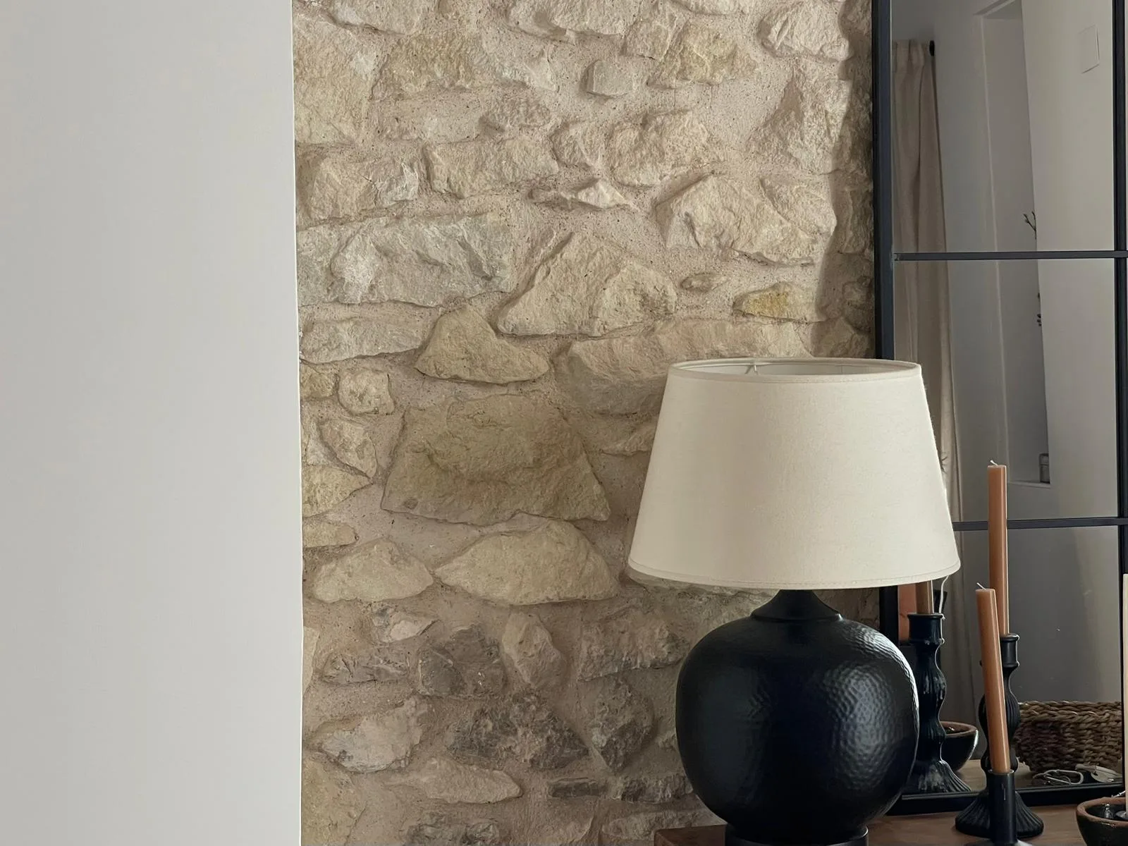 Techo de vigas de madera vista y muro de piedra encalado con una lámpara de cerámica negra