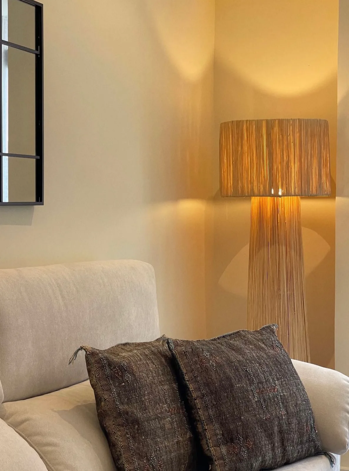Salón en tonos neutros con lámpara de fibra natural y sofá claro bañados por luz cálida